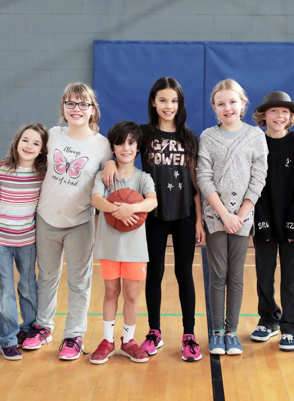 8 smiling kids of different ages standing in gymnasium together