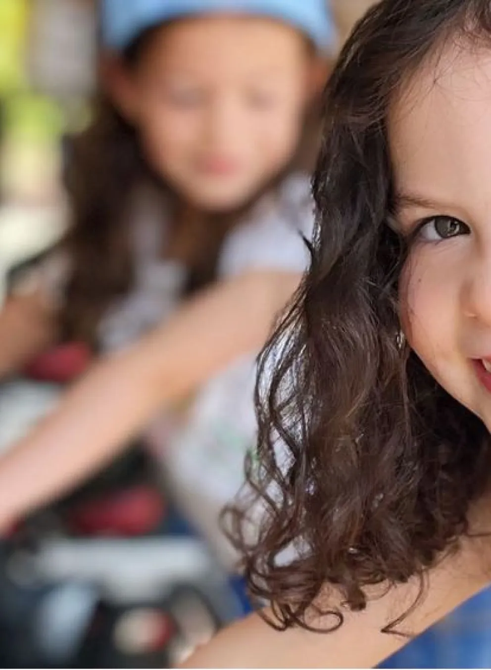A young girl is sitting on a cycle bike and smiling at the camera as an outdoor cycle class takes place behind her